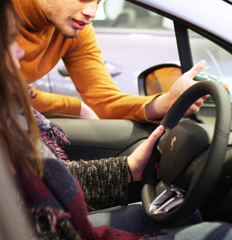 Une cliente assise au volant d'un véhicule et un vendeur présente