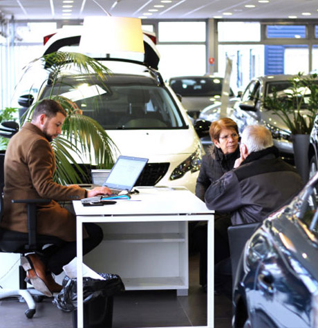 Des clients assis au bureau d'un vendeur dans une concession Peugeot